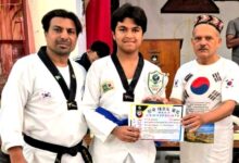 Three people at a martial arts ceremony: a young athlete of the National Taekwondo Club in a uniform holding a certificate between two coaches.