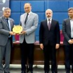 Federal Minister Ahsan Iqbal receiving a golden commemorative shield from AIOU Vice Chancellor Prof. Dr. Nasir Mahmood alongside other officials at an international conference ceremony.