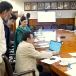 Punjab University Vice Chancellor Prof. Dr Muhammad Ali sitting at a conference table operating a laptop to launch the online affiliation portal, surrounded by faculty and committee members.