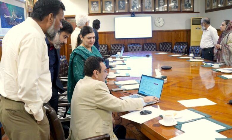 Punjab University Vice Chancellor Prof. Dr Muhammad Ali sitting at a conference table operating a laptop to launch the online affiliation portal, surrounded by faculty and committee members.