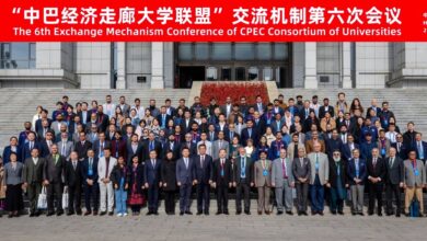 CPEC Consortium: A large group of over one hundred Chinese and Pakistani academics, university officials, and delegates standing together on the wide outdoor stone steps of a university building for a formal group photograph. The attendees, dressed in business suits, formal attire, and smart jackets, are arranged in multiple tiered rows. Above them, a bright red horizontal banner spans the top of the image featuring white Chinese and English text that reads, "The 6th Exchange Mechanism Conference of CPEC Consortium of Universities" along with "China · Harbin" and the date "2026.10.15".