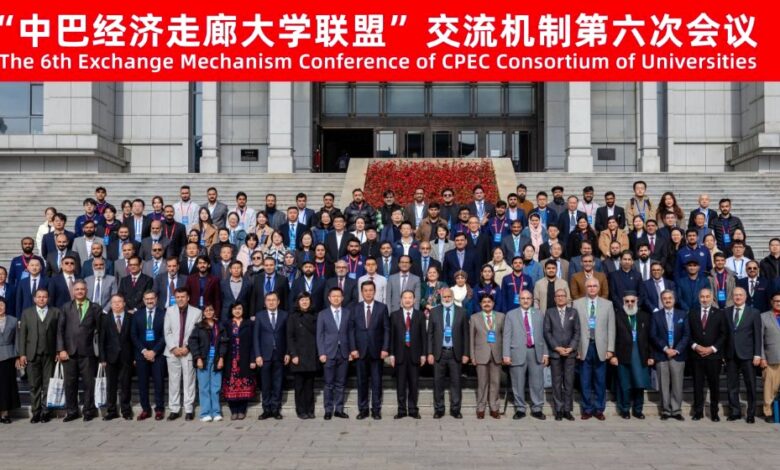 CPEC Consortium: A large group of over one hundred Chinese and Pakistani academics, university officials, and delegates standing together on the wide outdoor stone steps of a university building for a formal group photograph. The attendees, dressed in business suits, formal attire, and smart jackets, are arranged in multiple tiered rows. Above them, a bright red horizontal banner spans the top of the image featuring white Chinese and English text that reads, "The 6th Exchange Mechanism Conference of CPEC Consortium of Universities" along with "China · Harbin" and the date "2026.10.15".