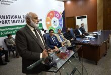 IRSIP Fellowship: Chairman HEC Dr Niaz Ahmad Akhtar addressing attendees at a glass podium during the IRSIP Batch 59 award ceremony, flanked by HEC officials and dignitaries seated on stage.