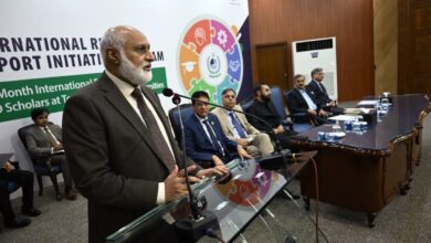IRSIP Fellowship: Chairman HEC Dr Niaz Ahmad Akhtar addressing attendees at a glass podium during the IRSIP Batch 59 award ceremony, flanked by HEC officials and dignitaries seated on stage.