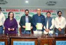 Roots Millennium Schools leadership and National Press Club officials standing behind a wooden desk, with Abdur Razzaq Sial and Dr Faisal Mushtaq holding signed green-and-white MoU documents in front of a National Press Club Islamabad backdrop.