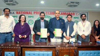 Roots Millennium Schools leadership and National Press Club officials standing behind a wooden desk, with Abdur Razzaq Sial and Dr Faisal Mushtaq holding signed green-and-white MoU documents in front of a National Press Club Islamabad backdrop.